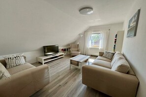 Ein modernes Wohnzimmer mit Fernseher, zwei Sofas, einem Couchtisch und einem Bücherregal.