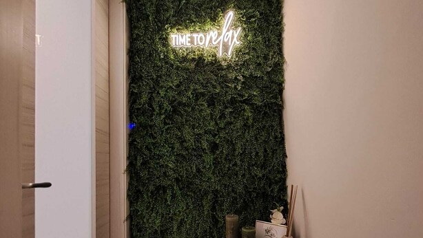 Un couloir avec un mur vert, un panneau lumineux néon indiquant « IL EST TEMPS D’ENVOYER UN FAX », et une petite table avec des bougies et une carte.