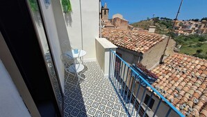 Un balcon avec des carreaux de sol à motifs, une petite table accompagnée d’une chaise, et une vue sur des bâtiments aux toits de tuiles en terre cuite.