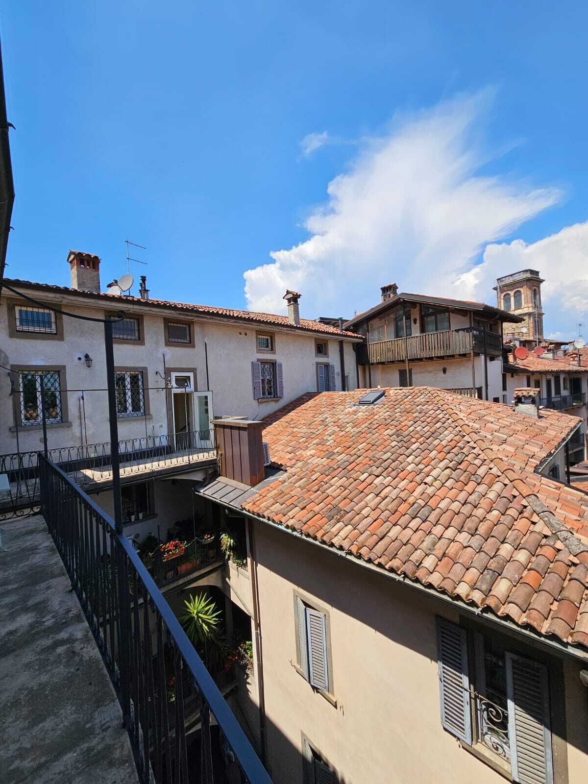 Un immeuble résidentiel doté d’un toit en tuiles, d’un balcon avec une rambarde en métal et d’un petit jardin agrémenté de plantes en pot.