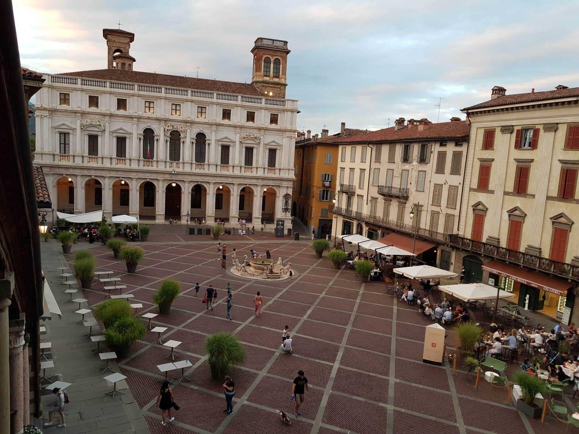 A courtyard with a fountain, outdoor seating, and a building with a clock tower.