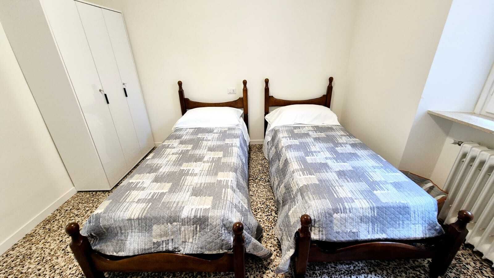 Une chambre avec deux lits en bois, une armoire blanche et un radiateur.