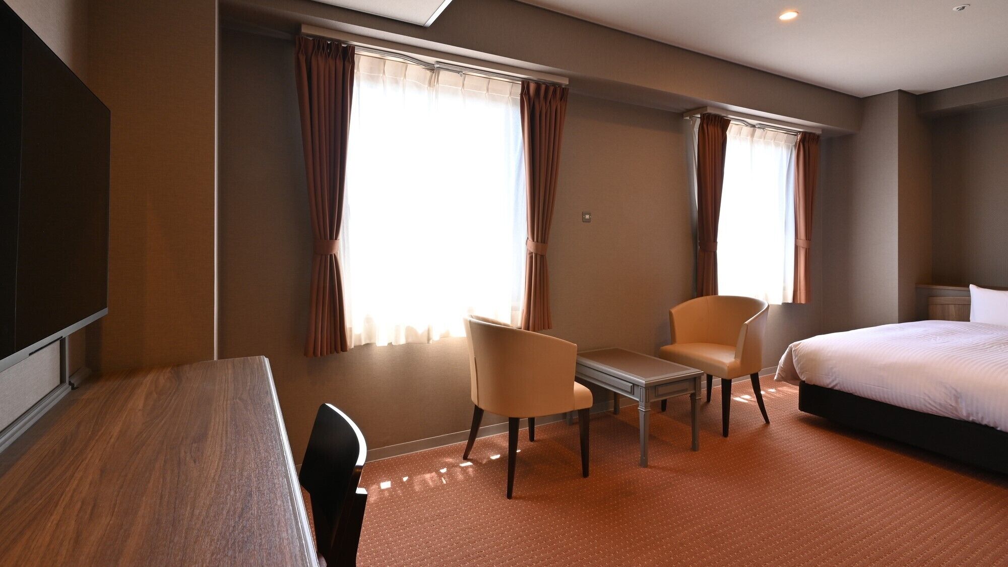 A hotel room with a bed, two chairs, a small table, and a TV.