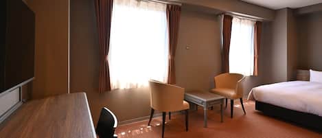 A hotel room with a bed, two chairs, a small table, and a TV.
