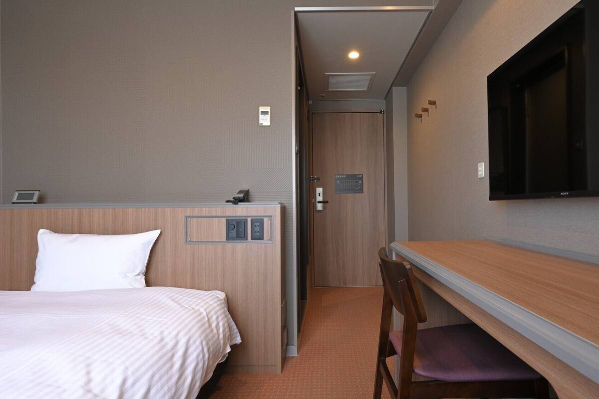 Una habitación de hotel con una cama, un escritorio, una silla, un televisor y una puerta.