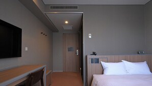 A hotel room with a bed, a desk, a chair, a television, and a door leading to another room.