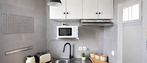 A compact kitchen with white cabinets, a microwave, a sink, a toaster, and a hanging pendant light.