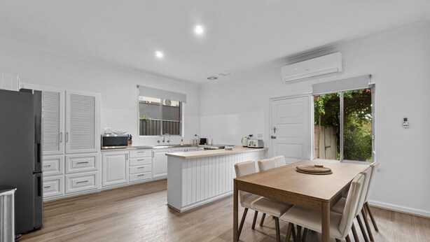 A modern kitchen with white cabinetry, a wooden dining table, and a large window. - Spacious 3-Bed Home in Payneham South (Payneham South)