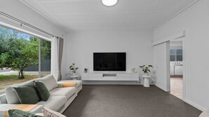 A modern living room with a flat-screen TV, a sofa, a coffee table, and a view of the outdoors. - Spacious 3-Bed Home in Payneham South (Payneham South)