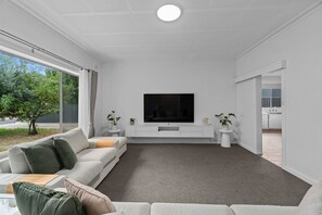 A modern living room with a flat-screen TV, a sofa, a coffee table, and a view of the outdoors. - Spacious 3-Bed Home in Payneham South (Payneham South)