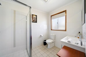 Ein Badezimmer mit Duschkabine aus Glas, Toilette, Waschbecken mit Spiegel und einem kleinen Mülleimer.