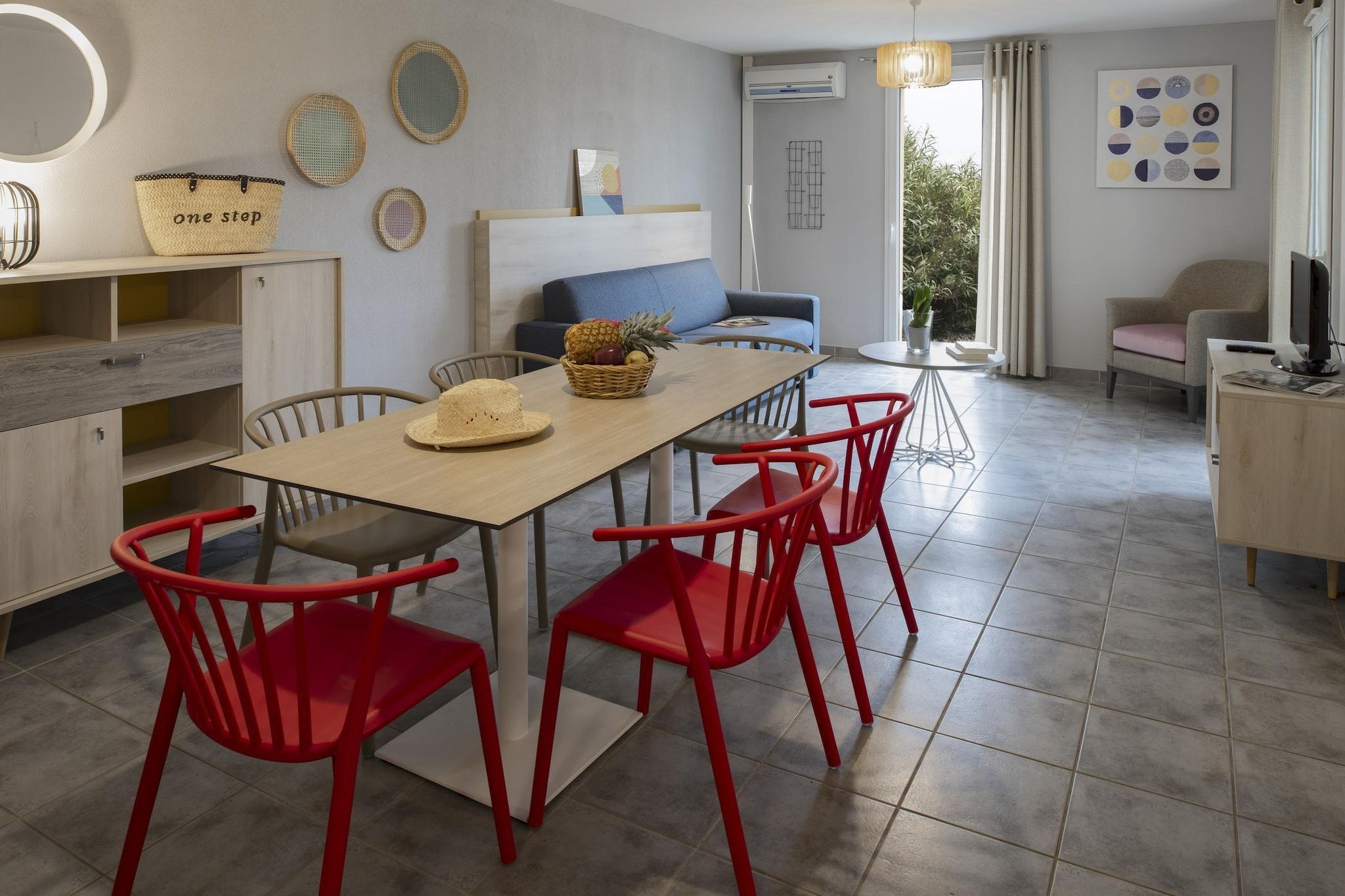 A modern kitchen with a dining table, red chairs, and a blue sofa.