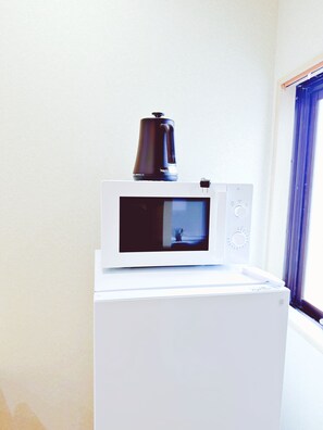 A white microwave with a black coffee pot on top, placed on a white appliance, likely a refrigerator, in a room with a window and a curtain. - Dc桜の苑-The Residence Tsurumibashi Shopping Arcade (Osaka)