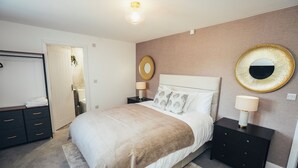 Een slaapkamer met een bed, nachtkastjes, een kaptafel, een spiegel en een deur.