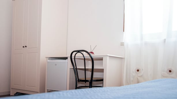 Un dormitorio con cama, escritorio y silla, armario y ventana con cortinas.