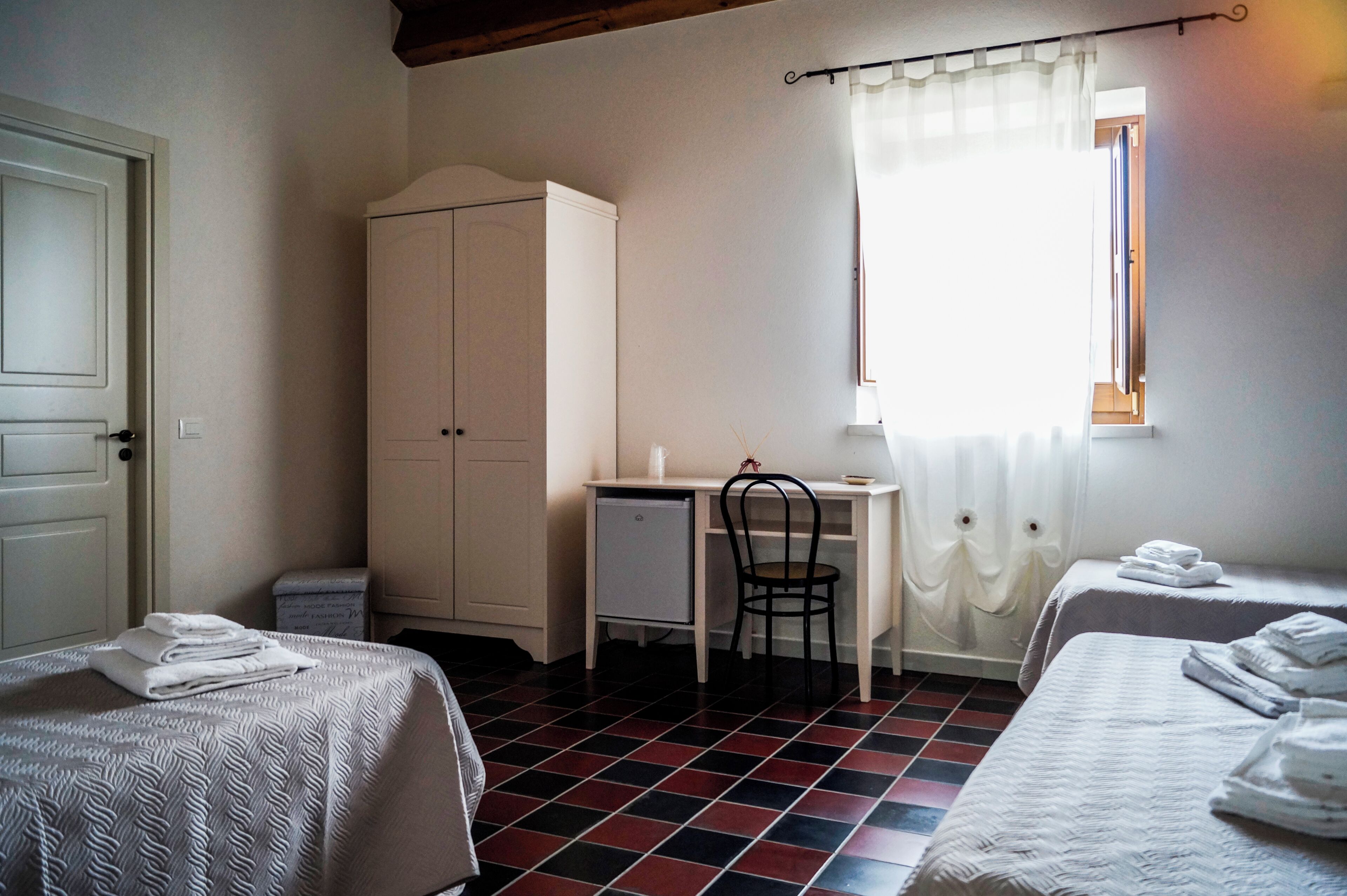 A room with two beds, a desk, a chair, a wardrobe, and a window with curtains.