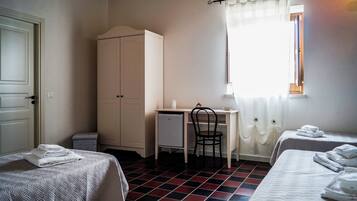 A room with two beds, a desk, a chair, a wardrobe, and a window with curtains.