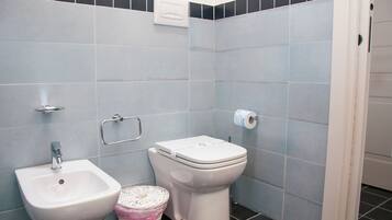 A bathroom with a bidet, toilet, and a hand dryer.