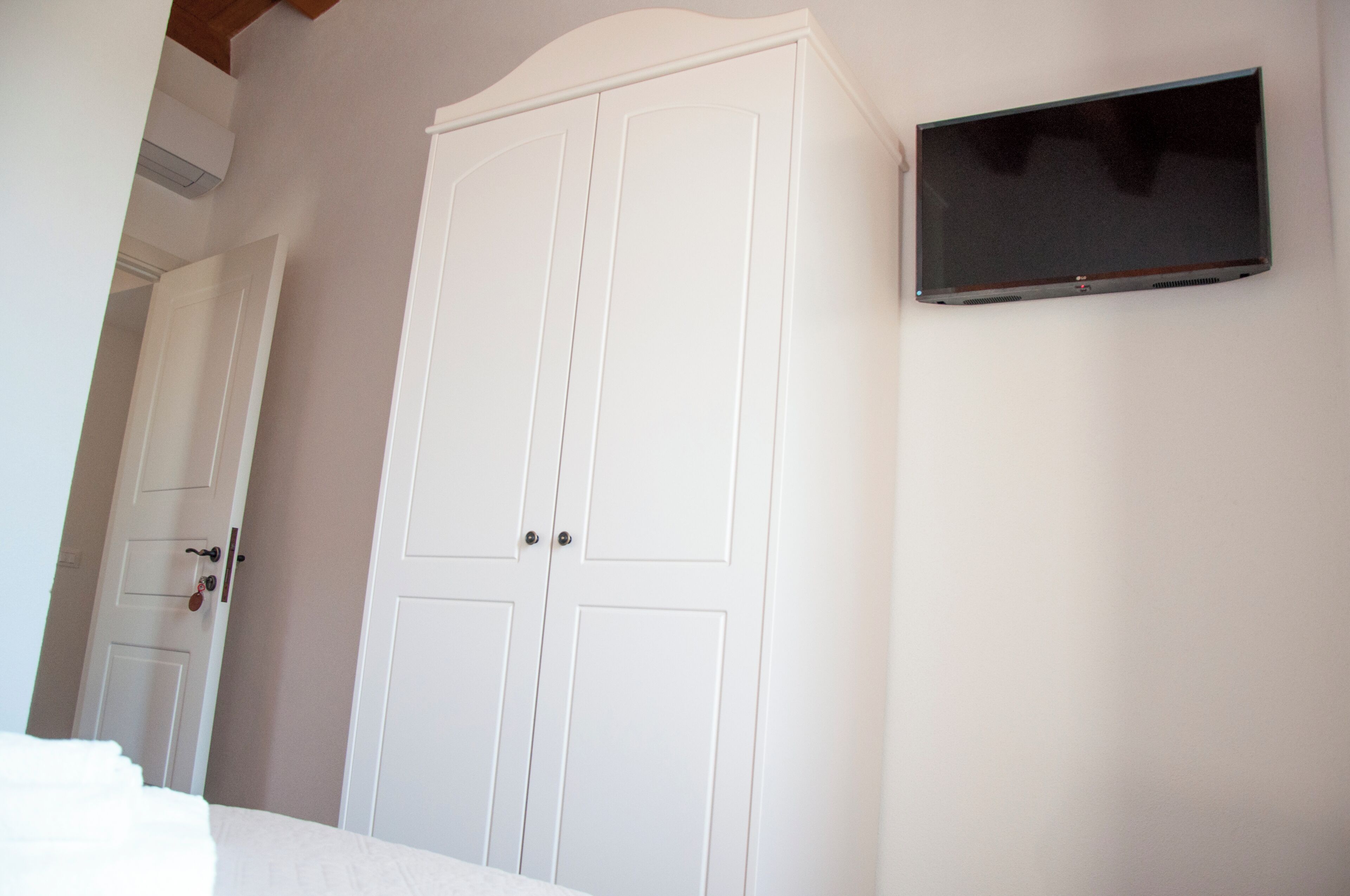 Een slaapkamer met een grote witte kast, een flatscreen televisie aan de muur en een deur naar een andere kamer.