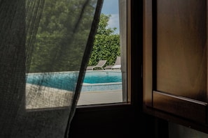 A window view of a swimming pool with lounge chairs and a tree. - Tre Balate Natura e Relax (Modica)