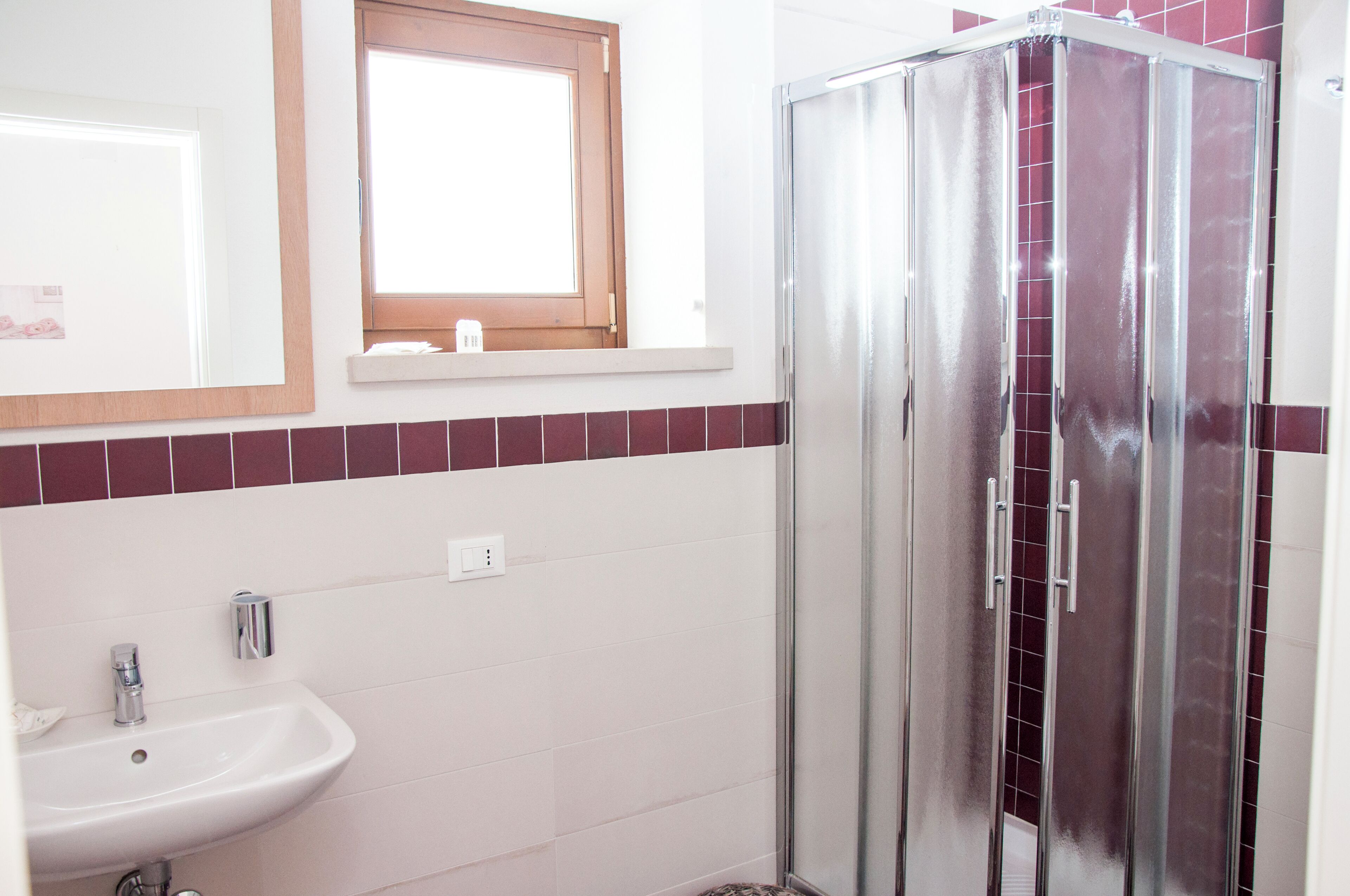 A bathroom with a sink, mirror, window, and shower.