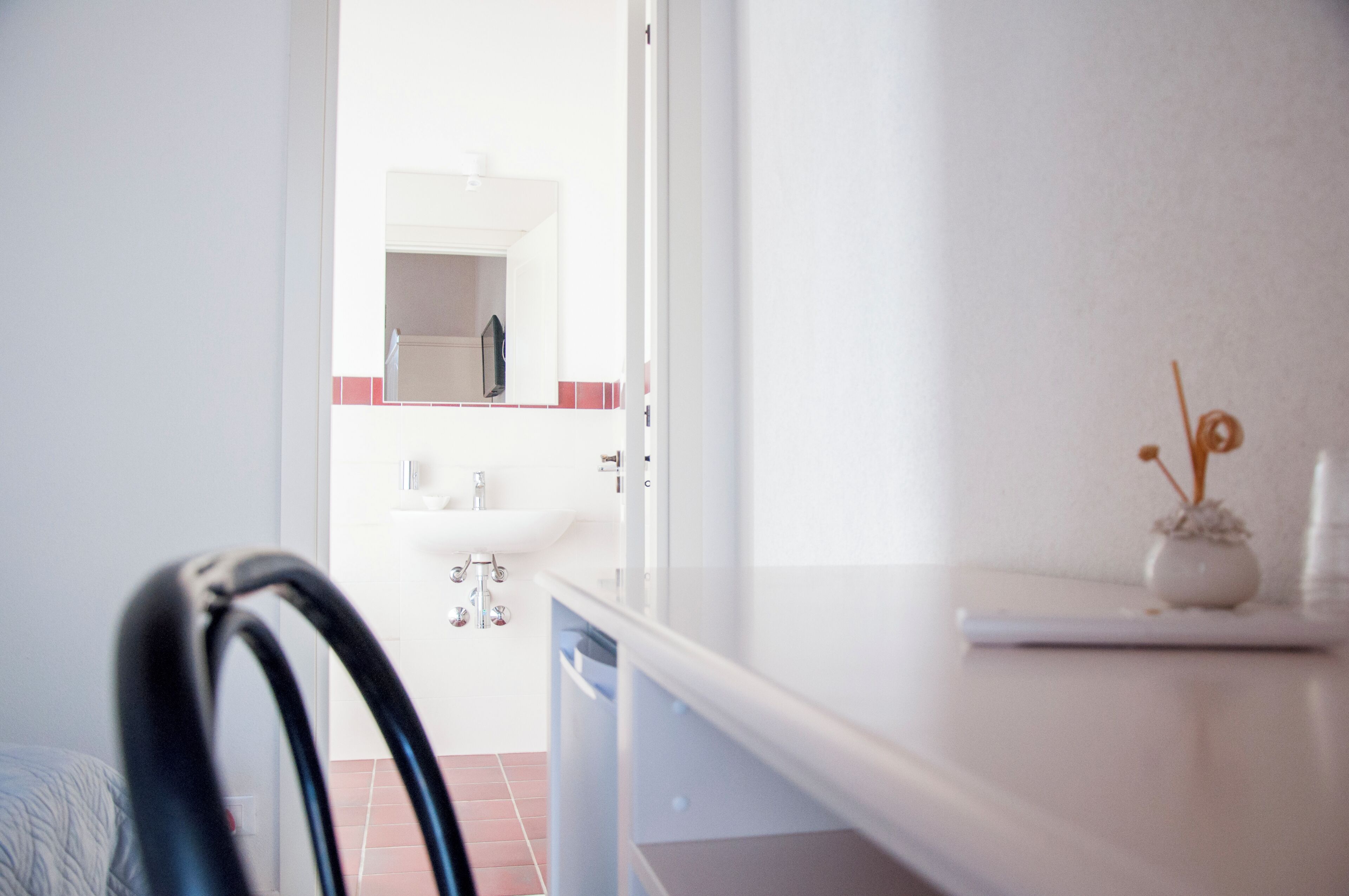 A hotel room with a white bathroom, a sink, and a small vase on the counter.