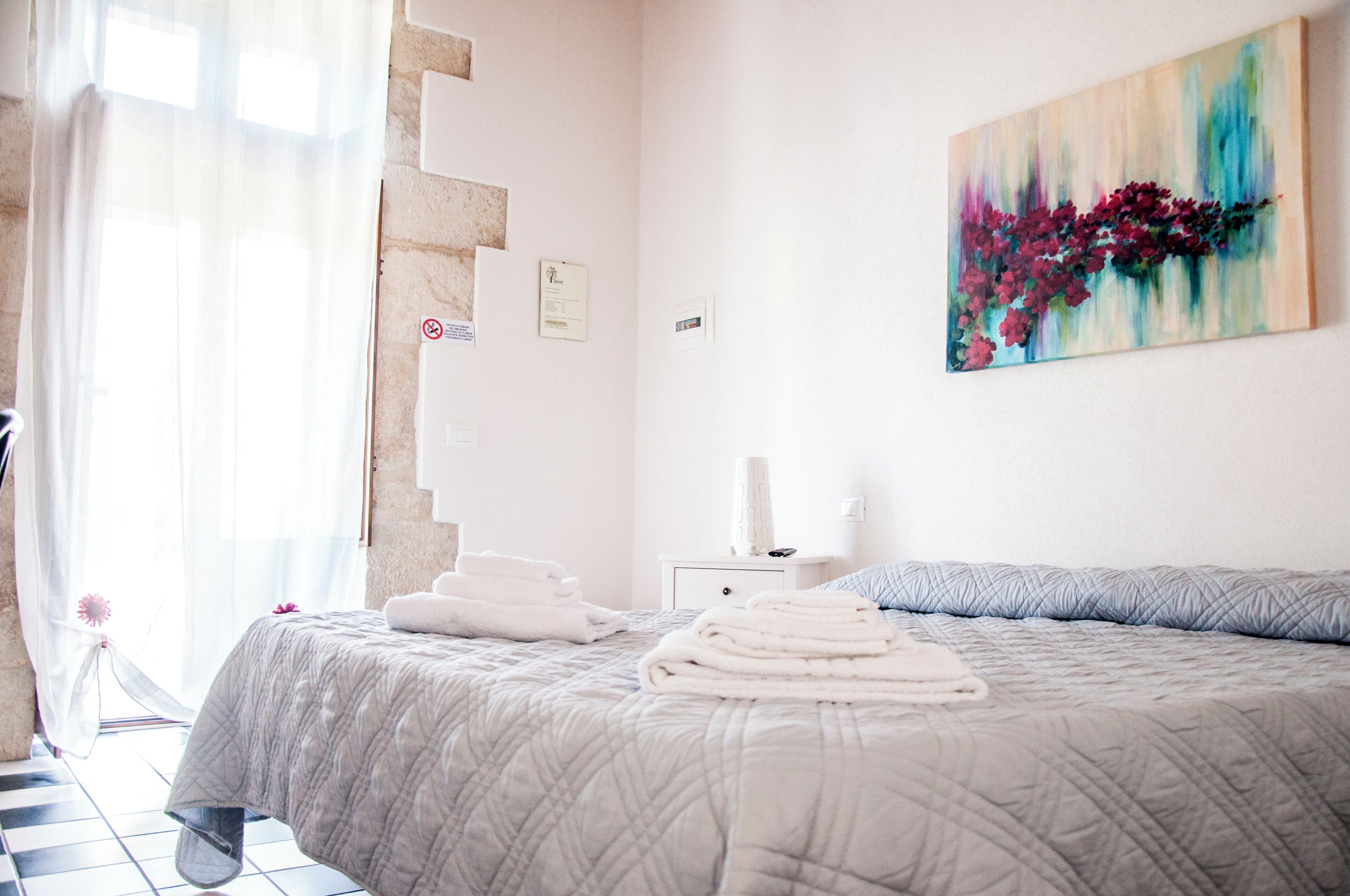 Quarto de hotel com cama, pintura, mesa de cabeceira e janela com cortinas.