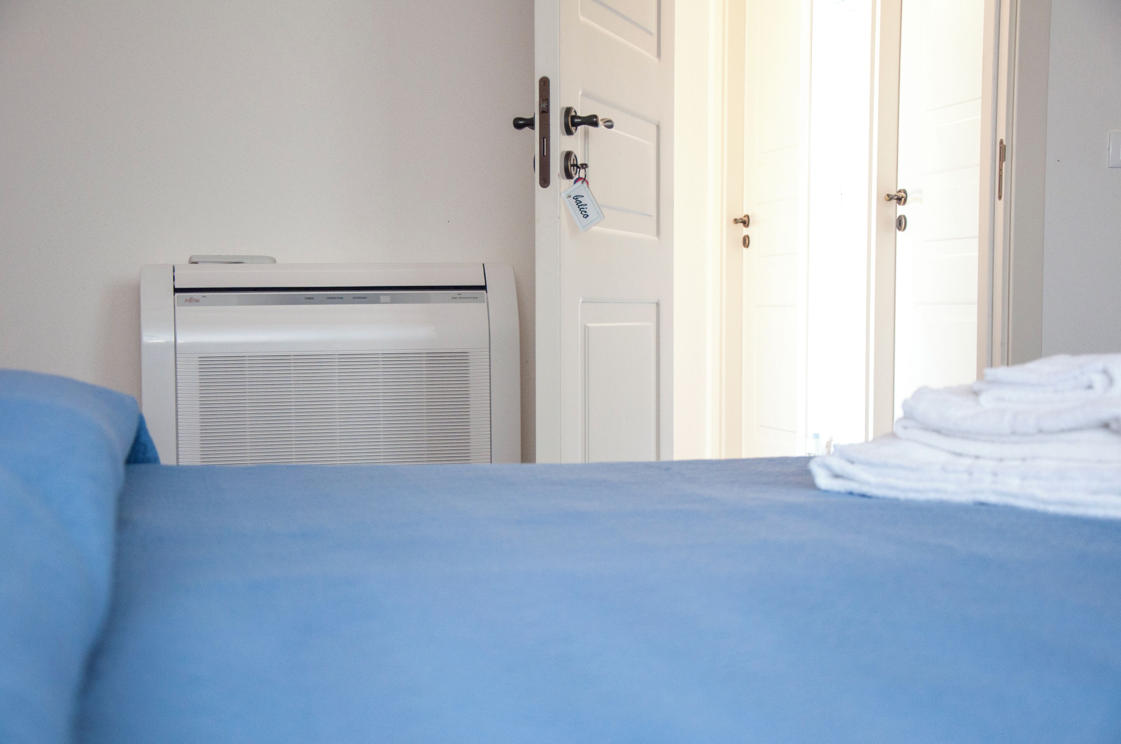 A hotel room with a bed, a white air conditioning unit, and a door with a key lock.
