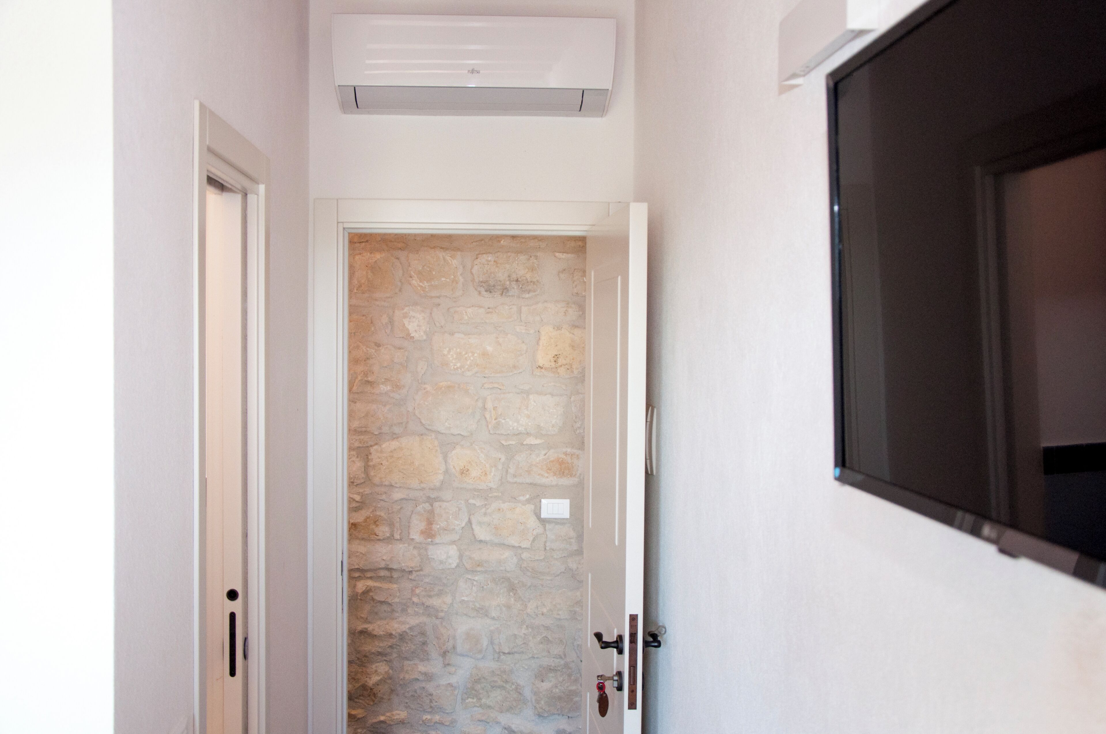 A hallway with a stone wall, a door, and a mounted TV.