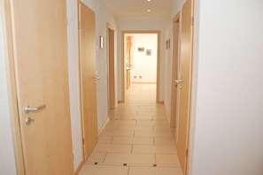 Ein Korridor mit Holztüren, Fliesenboden und Blick in einen Raum mit Bett und Fenster.