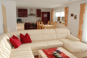 Ein Wohnzimmer mit einer Couch, roten Kissen, einem Couchtisch und einem Essbereich mit Tisch und Stühlen.