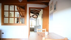 Ein Zimmer mit Holztisch und -stühlen, einem Fenster mit Holzrahmen und einer Tür zu einem anderen Raum.