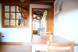 Una stanza con un tavolo e sedie in legno, una finestra con stipiti in legno e una porta che dà su un'altra stanza.