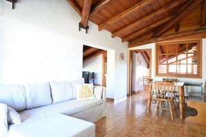 Un soggiorno con un divano bianco, travi a vista in legno, un'area pranzo con sedie in legno e una finestra con vista.