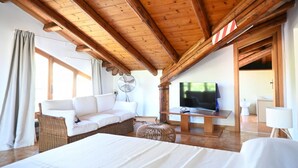 Ein Hotelzimmer mit Holzboden, einer Couch, einem Fernseher, einem Bett und einem Fenster.