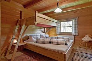 Ein Schlafzimmer in einer Holzhütte mit Schlafkoje, einer Leitern und einem Fenster mit Vorhängen sowie einem kleinen Stuhl.