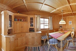 Ein Holzhütten-Innenraum mit Esstisch, Stühlen und einer Küchenzeile mit Schränken und einem Fenster.