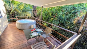 A wooden deck with a table and chairs, a hot tub, and lush greenery.