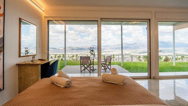 Ein Schlafzimmer mit einem großen Bett, einem Schreibtisch und Blick auf eine grüne Landschaft durch große Schiebetüren.