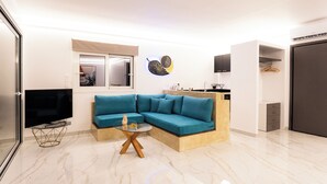 Ein modernes Wohnzimmer mit einer Eckcouch, einem Glastisch, einem Flachbildfernseher und einer Küchenzeile mit Schränken und Arbeitsplatte.