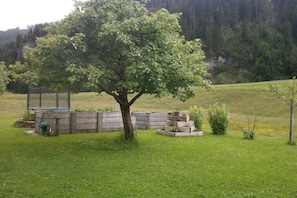 Ein Baum in einer grünen Wiese mit einem Holzen Bauwerk in der Nähe.