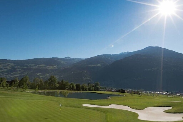 Ein Golfplatz mit Fahne, Teich und Bergen im Hintergrund.