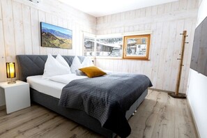 Ein Schlafzimmer mit Bett, Nachttisch, Lampe, Fenster und einem Bild an der Wand.