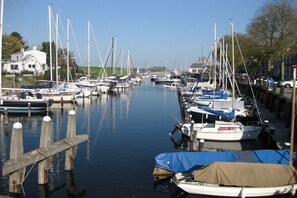 Ein Yachthafen mit mehreren Booten, die an einem ruhigen Wasserweg liegen, Holzstegen und Gebäuden im Hintergrund.