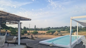 A swimming pool with a wooden deck, a covered seating area, and a view of the surrounding landscape. - Farmhouse CASA AYO (Santiago do Cacém)