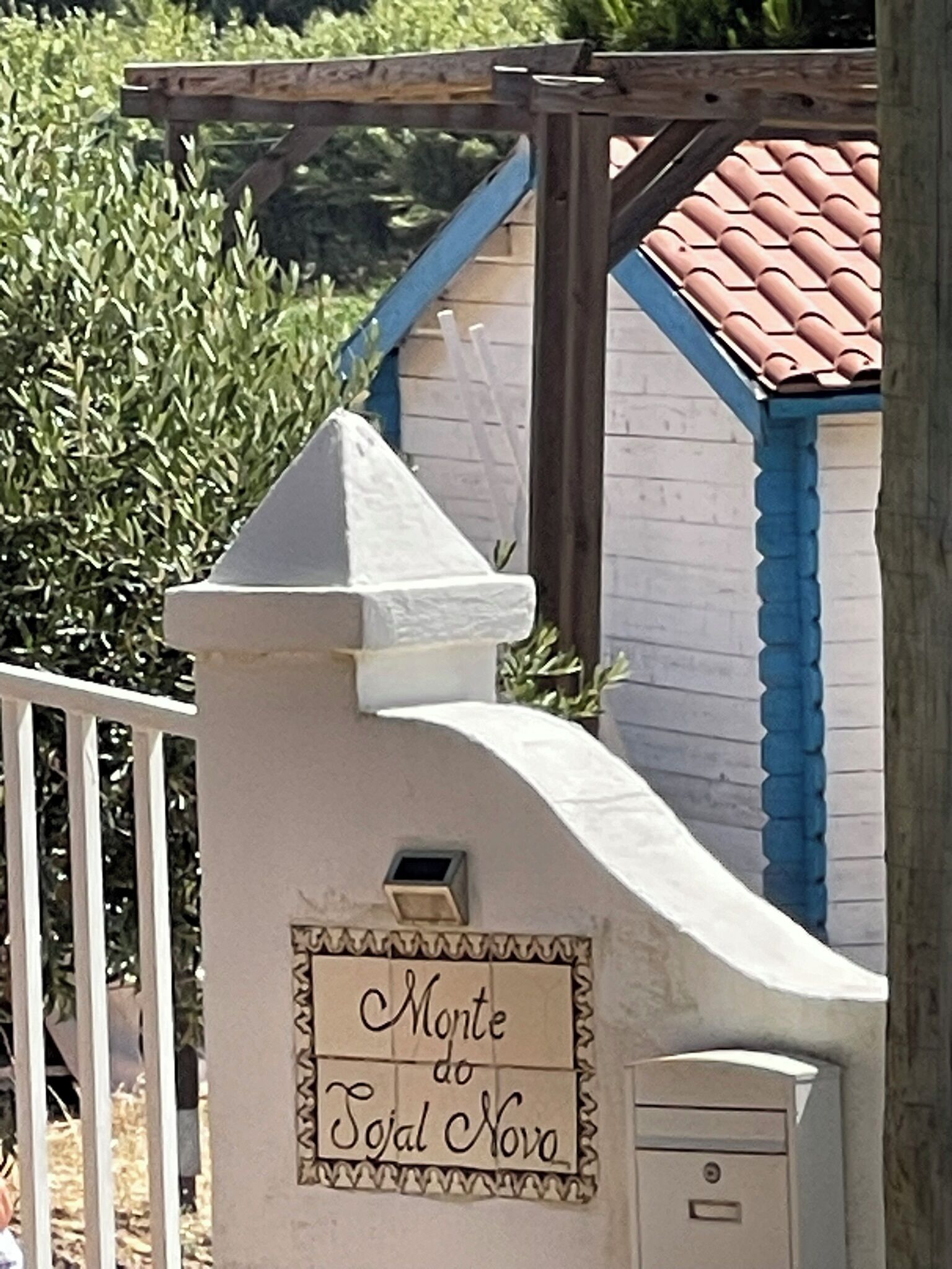 A white building with a sign reading 'Monte do Tójal Novo' and a metal gate.