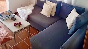 A living room with a sofa, a small table, a decorative mirror, and a window with curtains. - Farmhouse CASA AYO (Santiago do Cacém)