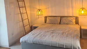 A bedroom with a wooden ceiling, a bed with a grey headboard, two bedside lamps, and a ladder against the wall. - Farmhouse CASA AYO (Santiago do Cacém)