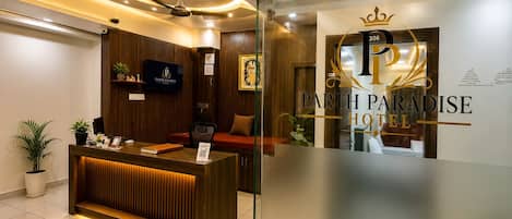 Una recepción con detalles de madera, un televisor montado en la pared y un cartel con el nombre del hotel, 'Parth Paradise Hotel'.