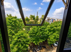 Vista a través de una ventana que muestra una zona residencial con árboles, cielo despejado y edificios al fondo.